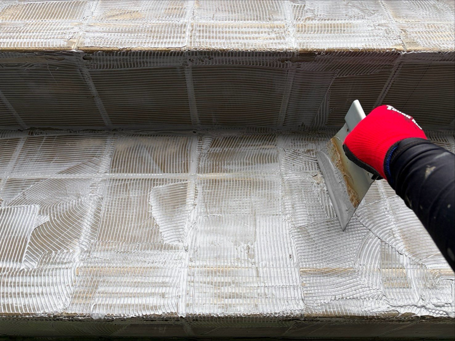施工中:クシ目ゴテで下地に接着剤を塗布する様子