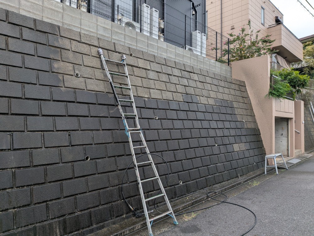 脚立を使って擁壁を高圧洗浄しているようす